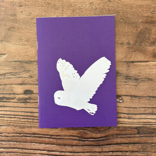 Purple notebook with a white barn owl design on a wooden surface