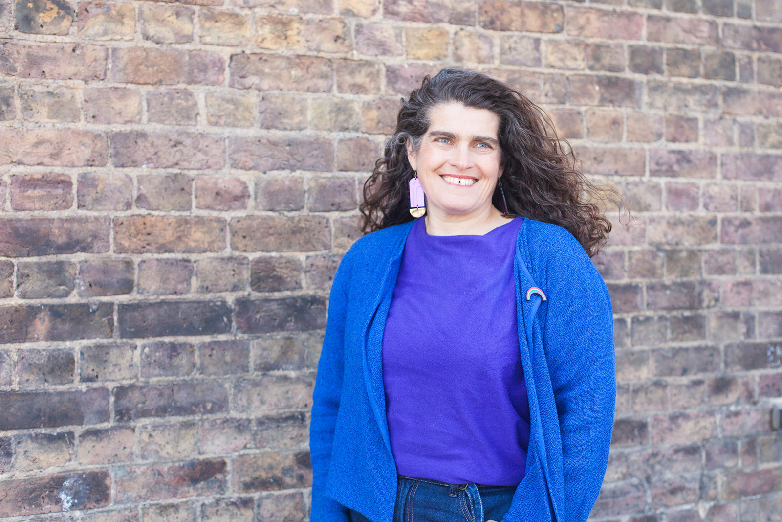 Paula, UmmPixies Founder wearing brightly coloured jacket standing against a brick wall