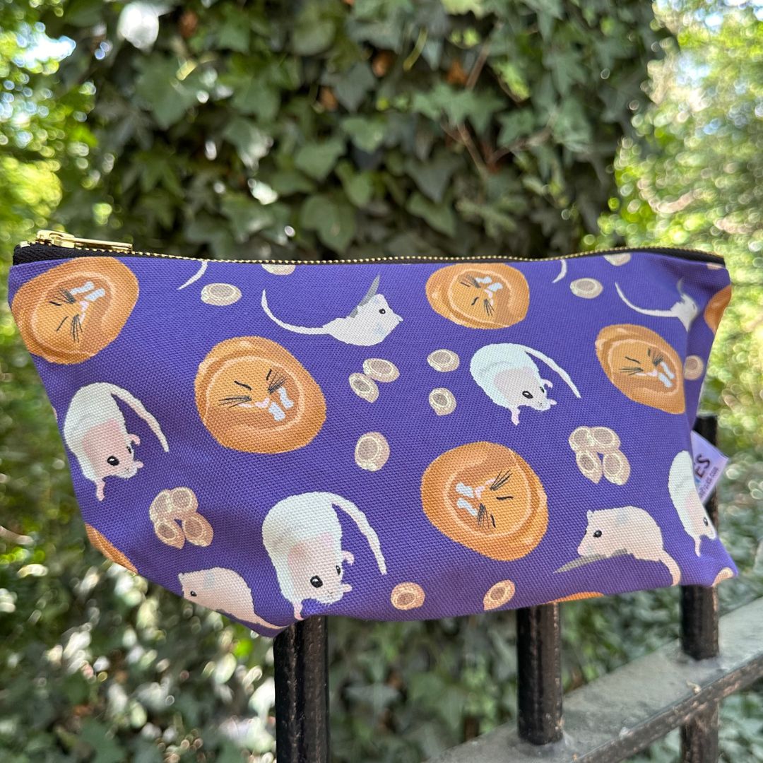 A purple zippered pouch with a playful print of dormice photographed outdoors on a black metal railing with green ivy in the background.