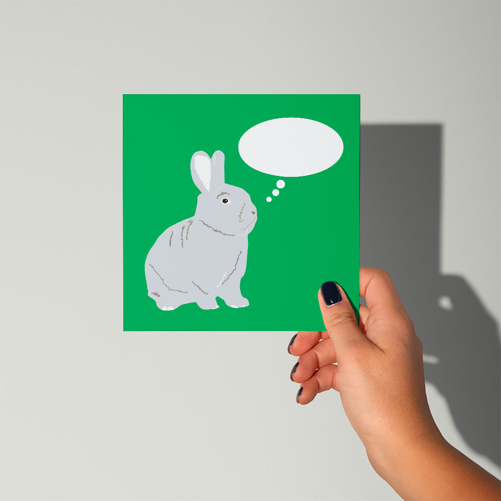 Hand holding a green card with a rabbit illustration and thought bubble on a gray background
