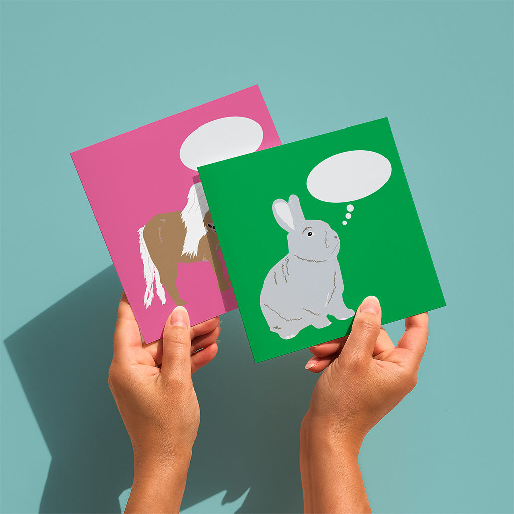 Two hands holding pink and green cards with animal illustrations on a teal background