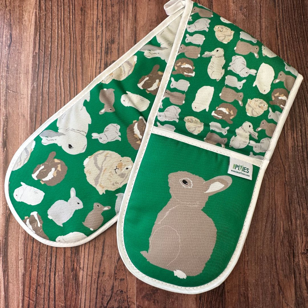 Bright Green Rabbits design organic cotton Oven Mitts shown with left mitt with wild rabbit illustration uppermost on a wooden counter