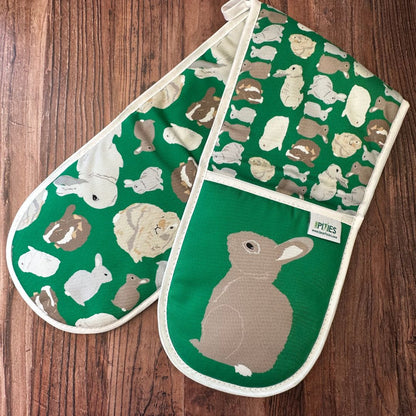 Bright Green Rabbits design organic cotton Oven Mitts shown with left mitt with wild rabbit illustration uppermost on a wooden counter
