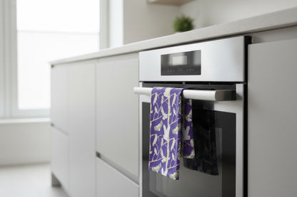 Colourful purple organic cotton tea towel with illustrations of British owls including the bran owl  shown hanging over the door of an oven in a modern kitchen