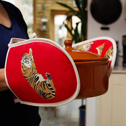 Person holding a pot with tiger-themed red oven mitts in a kitchen setting