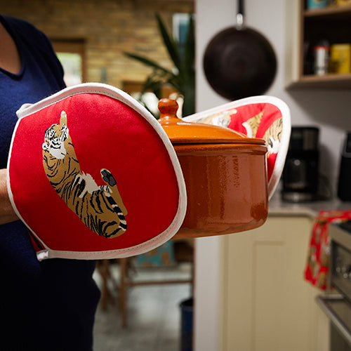 Person holding a pot with red tiger-themed oven mitts in a kitchen setting