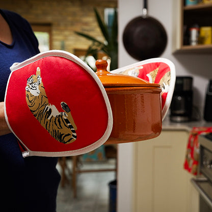 Person holding a pot with red tiger-themed oven mitts in a kitchen setting