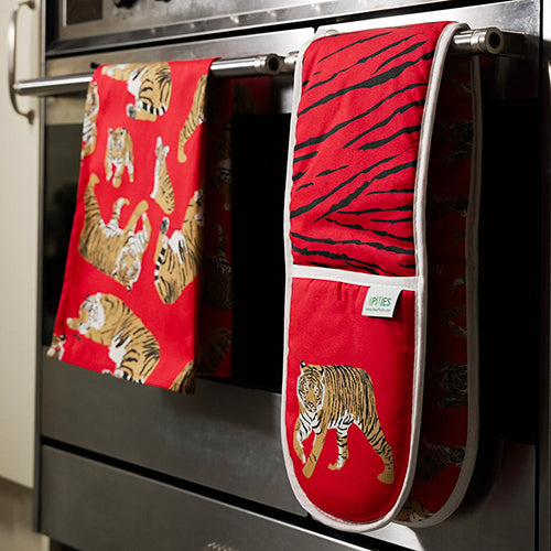 Red tiger-themed kitchen towel and oven mitt hanging on a stove handle.