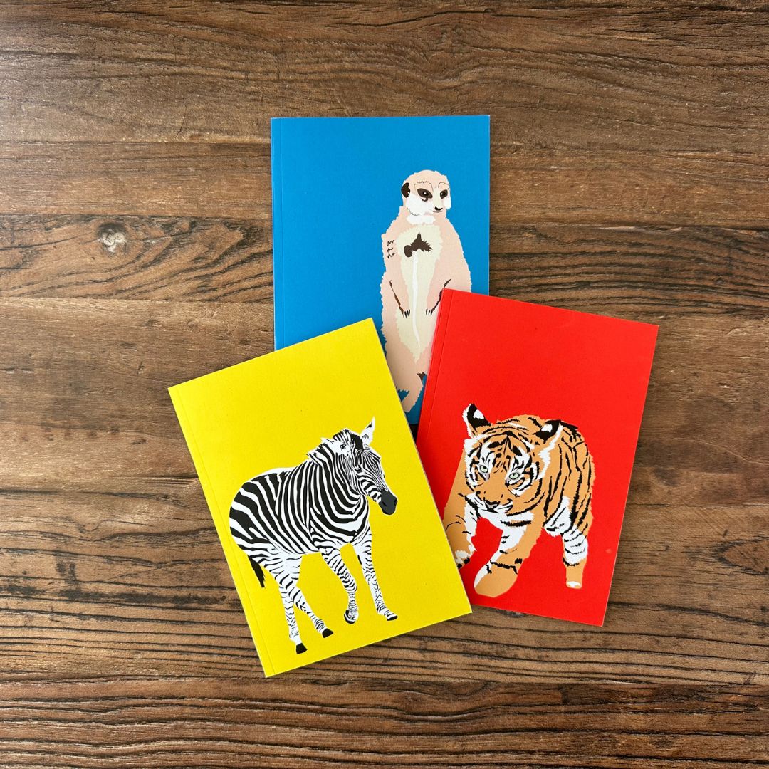 Three colourful pocket notebooks cards with animal illustrations on a wooden surface