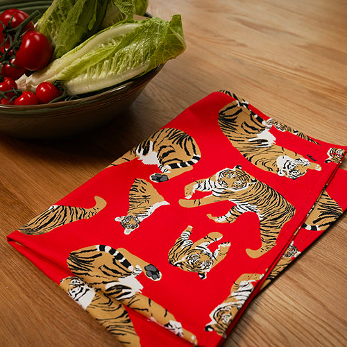 Red tea towel with tiger pattern on a wooden table next to a bowl of salad.