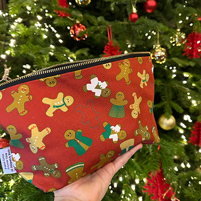 Red pouch with gingerbread man pattern held in front of a decorated Christmas tree.