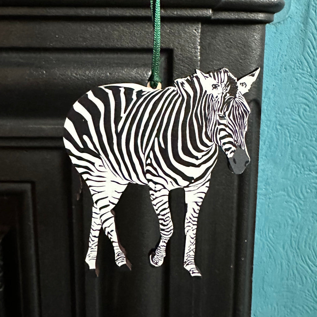 Wooden Zebra hanging decoration shown hanging on edge of cast iron fireplace