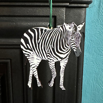 Wooden Zebra hanging decoration shown hanging on edge of cast iron fireplace