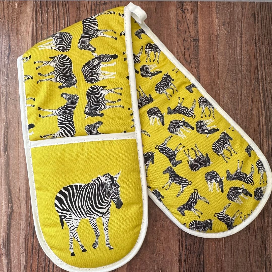 Yellow Zebra illustrated organic cotton oven gloves on wooden surface showing inside printed pattern of scattered zebras