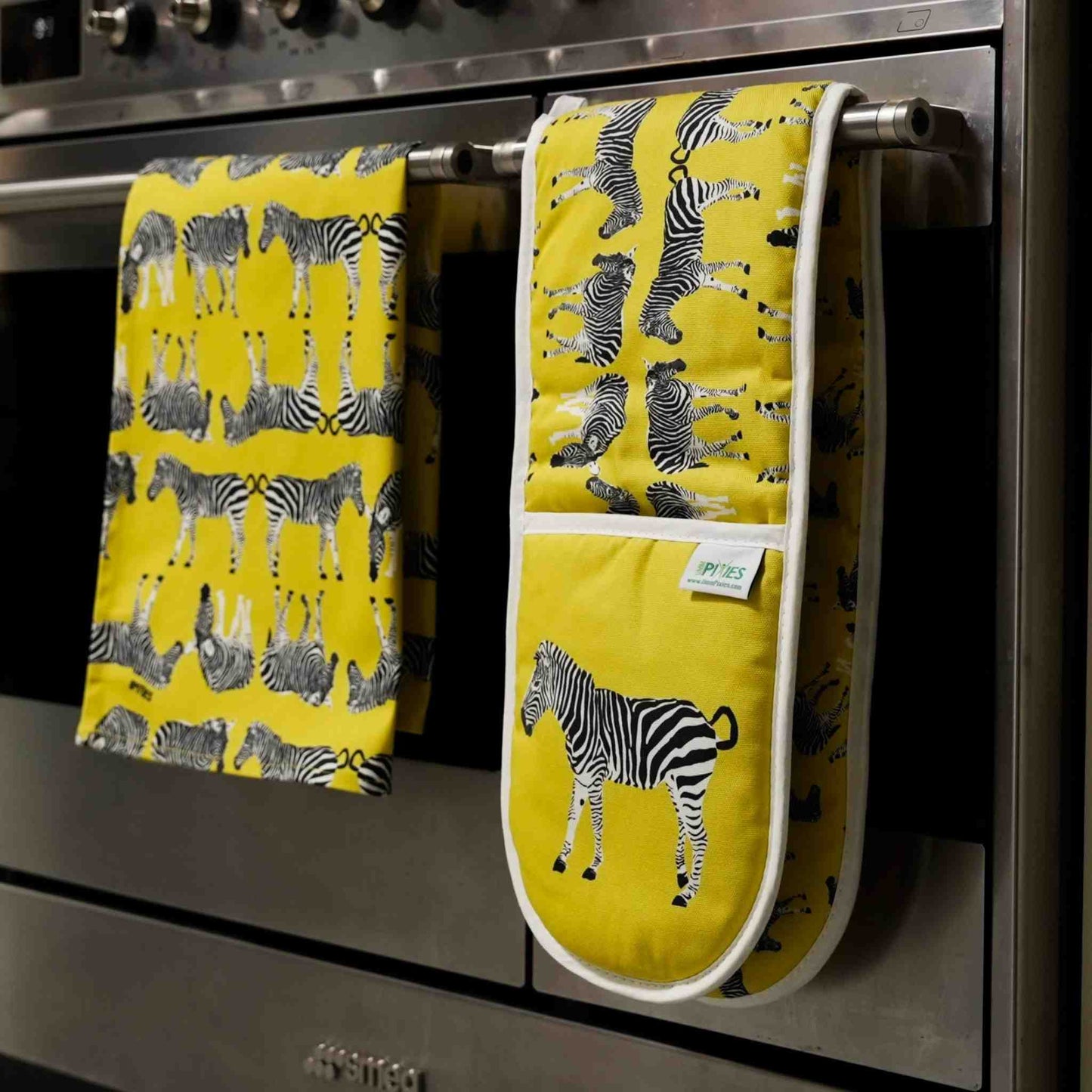 Yellow kitchen towel and oven mitt with zebra pattern hanging on a stove handle.