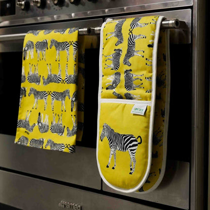 Yellow kitchen towel and oven mitt with zebra pattern hanging on a stove handle.