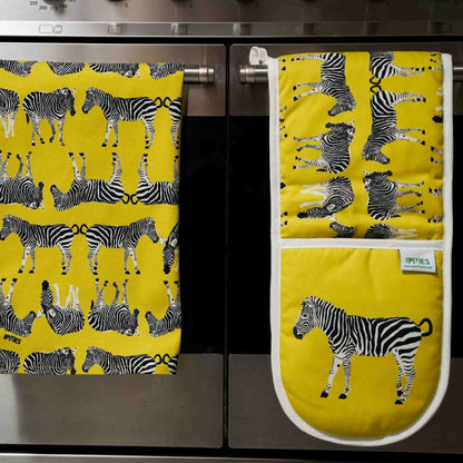 Yellow kitchen towel and matching oven gloves with zebra pattern on a kitchen stove.