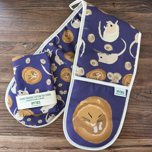 Rich Purple Hazel Dormouse design organic cotton Oven Mitts shown with matching tea towel on a wooden counter