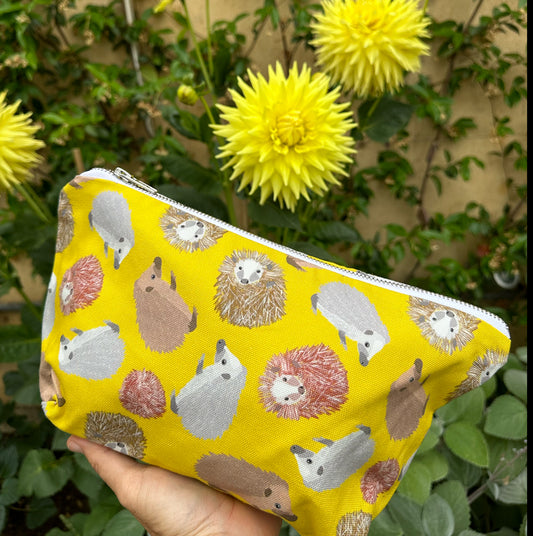 Yellow hedgehog patterned really useful bag shown held in hand in front of yellow flower