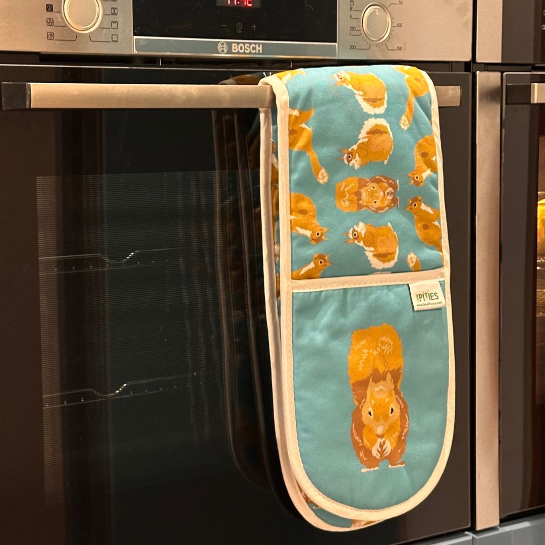 A teal oven mitt with a squirrel design hangs from the handle of a built-in oven. 