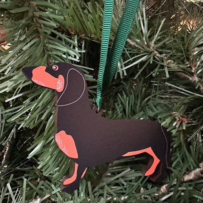 Dog-shaped Christmas ornament on a green ribbon against a pine tree background