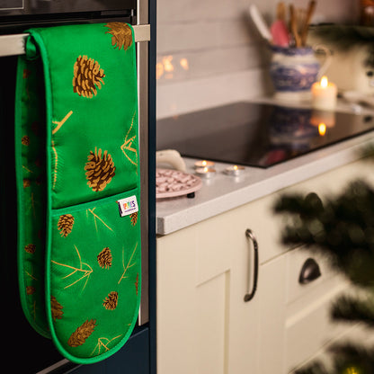 A pair of green double oven mitt with illustrations of Douglas fir cones and spruce sprigs shown handing over an oven door handle