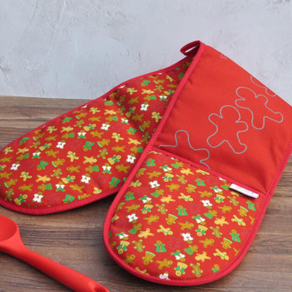 Burgundy organic cotton double oven mitts with UmmPixies' gingerbread folk design. shown on a wooden kitchen counter