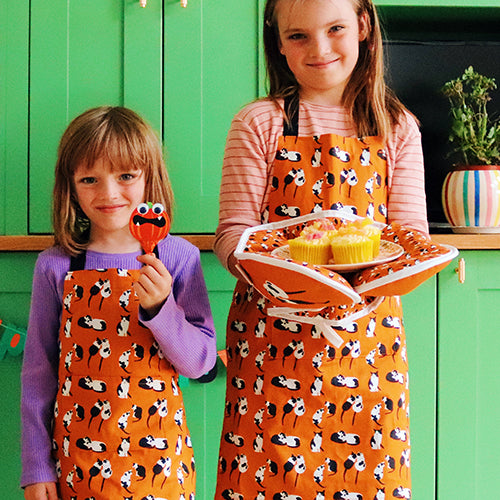 Orange Black and White Cats Design Organic Cotton Apron, models wear younger child and older child sizes matching oven gloves also shown
